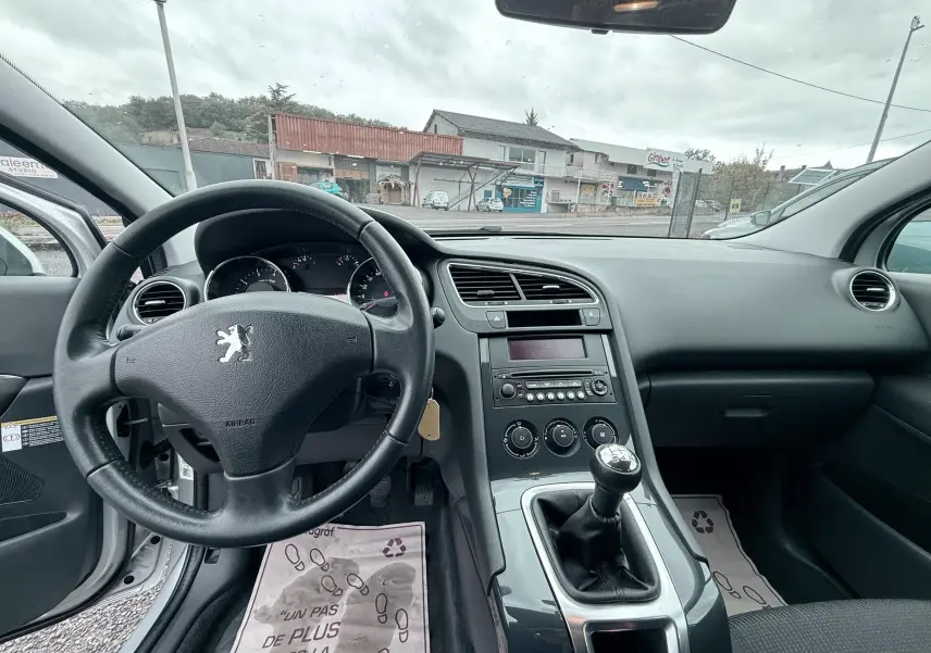 Vue intérieure du tableau de bord et volant en cuir noir d'une Peugeot 5008 2010 avec boîte manuelle, ambiance sobre et fonctionnelle.