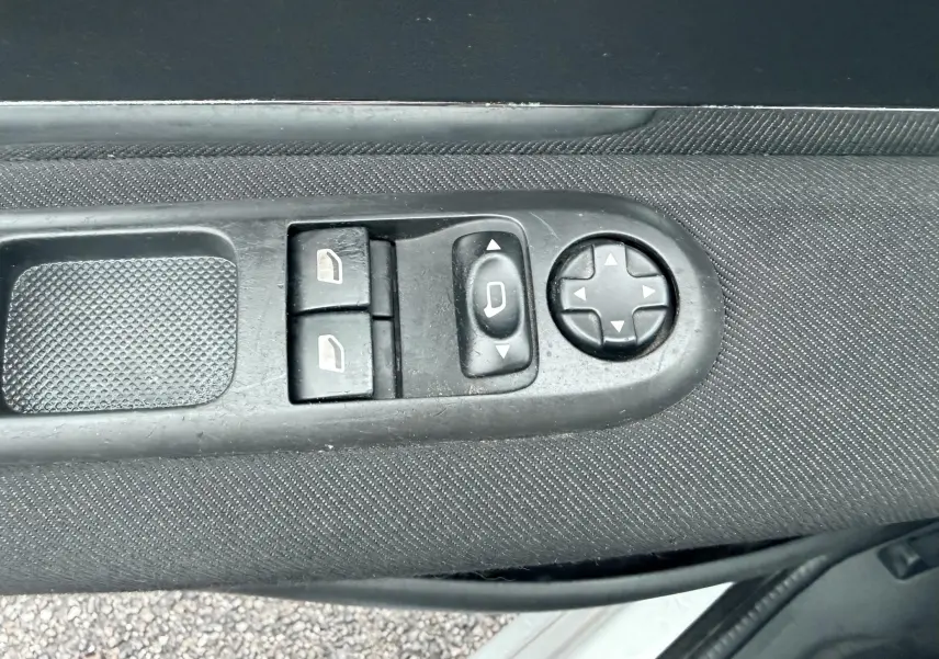Gros plan sur les commandes de réglage des vitres et des rétroviseurs sur la porte côté conducteur d’un Peugeot 5008 gris.