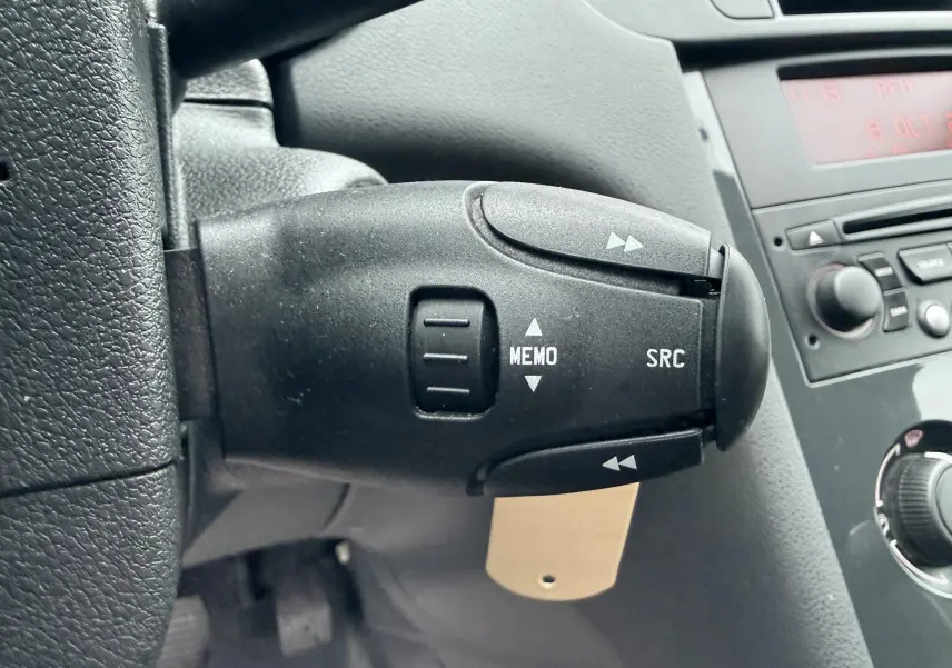 Gros plan sur la commande au volant gauche du Peugeot 5008 gris, avec boutons MEMO et SRC visibles.