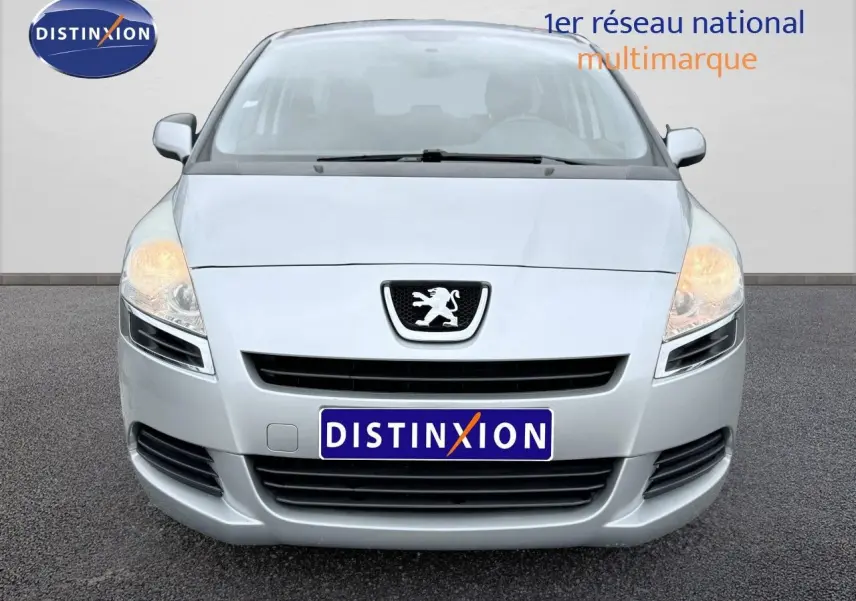 Vue frontale d'un Peugeot 5008 gris avec phares allumés sur fond neutre.