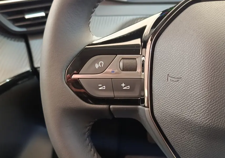 Gros plan sur les commandes gauche du volant cuir noir du Peugeot 208 électrique blanc, avec boutons multifonctions.