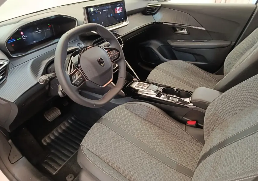 Vue intérieure avant droite de la Peugeot 208 électrique 2024 avec sièges gris et tableau de bord numérique.