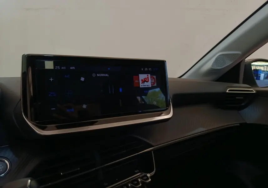 Vue rapprochée de l’écran tactile central noir et du tableau de bord du Peugeot 208 électrique blanc, intérieur moderne.