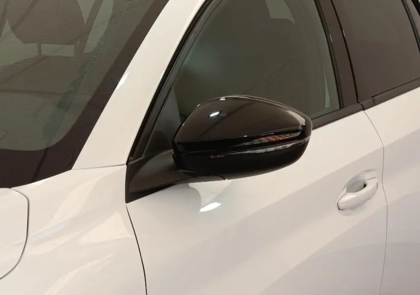 Gros plan sur le rétroviseur noir côté conducteur d’une Peugeot 208 électrique blanche 2024, avec poignée de porte visible.
