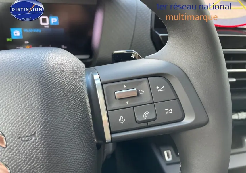 Gros plan sur les commandes au volant à droite de la Citroën C4 2024, finition gris platinium métal, avec affichage numérique en arrière-plan.