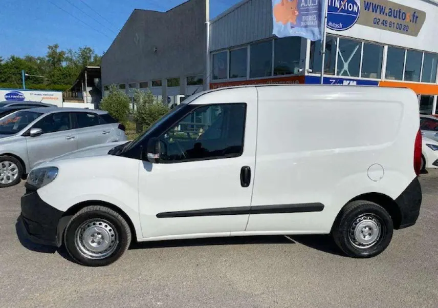 Vue de profil côté gauche d'un utilitaire FIAT Doblo blanc avec porte latérale droite et pare-chocs noirs non peints.