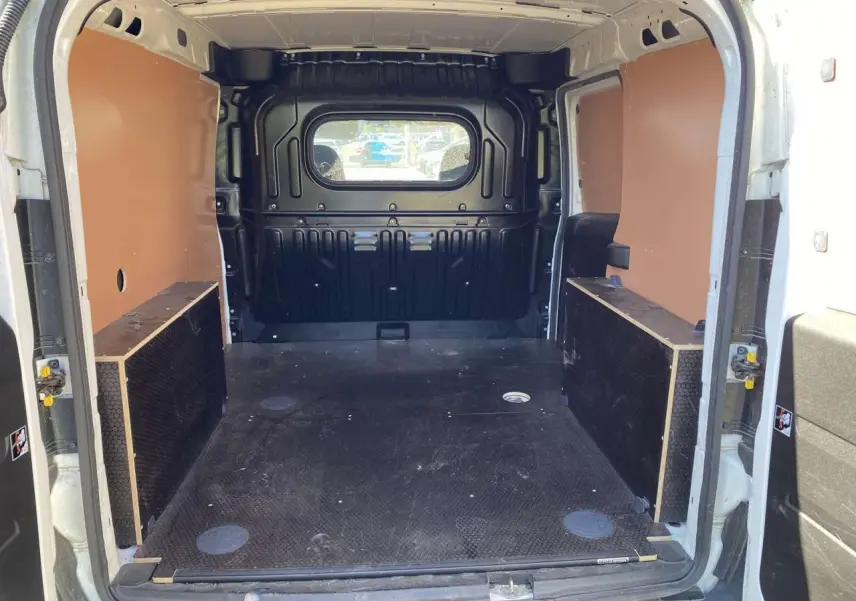 Vue intérieure arrière du fourgon blanc FIAT Doblo 2017, montrant l'espace de chargement avec kit bois et paroi vitrée.