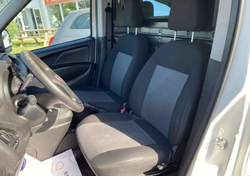 Vue intérieure côté conducteur du Fiat Doblo blanc 2017 montrant les sièges avant et la paroi vitrée de séparation.