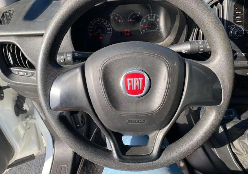 Vue rapprochée du volant noir avec logo FIAT rouge dans l'habitacle d'un Fiat Doblo blanc de 2017.