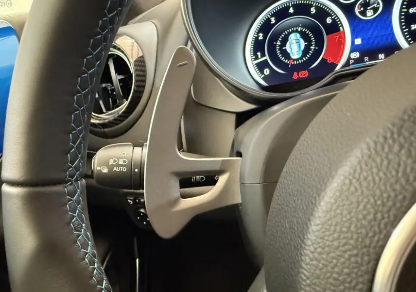 Gros plan sur le volant cuir noir avec surpiqûres bleues et les commandes du tableau de bord numérique de l'Alpine A110 Legende 2019.