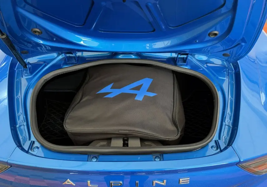 Vue plongeante sur le coffre avant ouvert d'une Alpine A110 Legende bleue avec sac de rangement noir marqué du logo bleu.