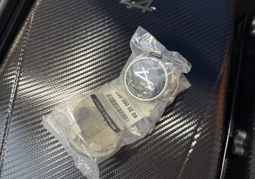 Gros plan sur un badge Alpine A110 emballé posé sur une surface en fibre de carbone à l'intérieur du véhicule.