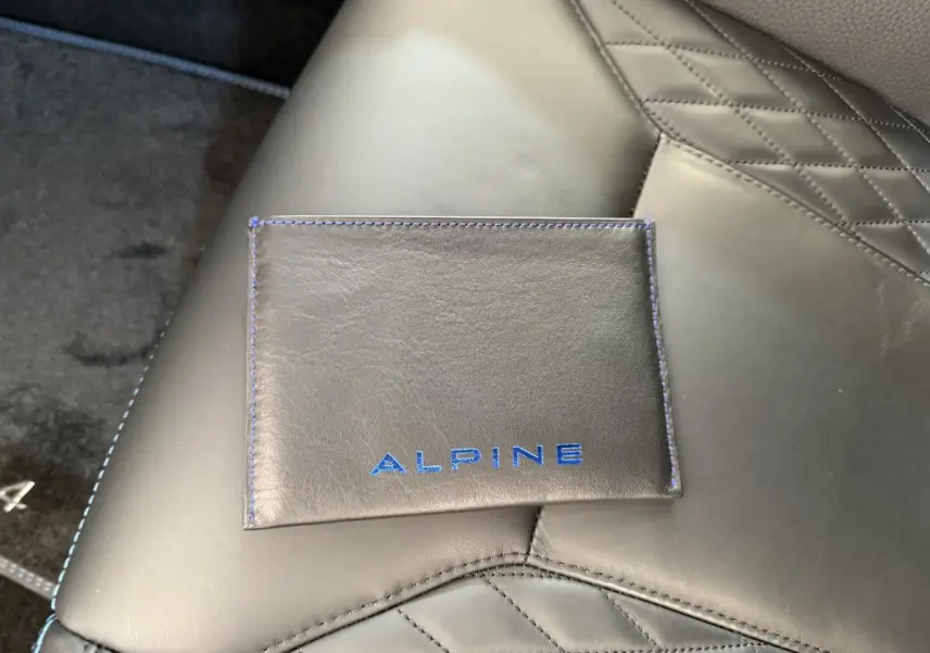 Gros plan sur une pochette Alpine noire avec coutures bleues posée sur un siège en cuir noir matelassé de l'Alpine A110 Legende 2019.