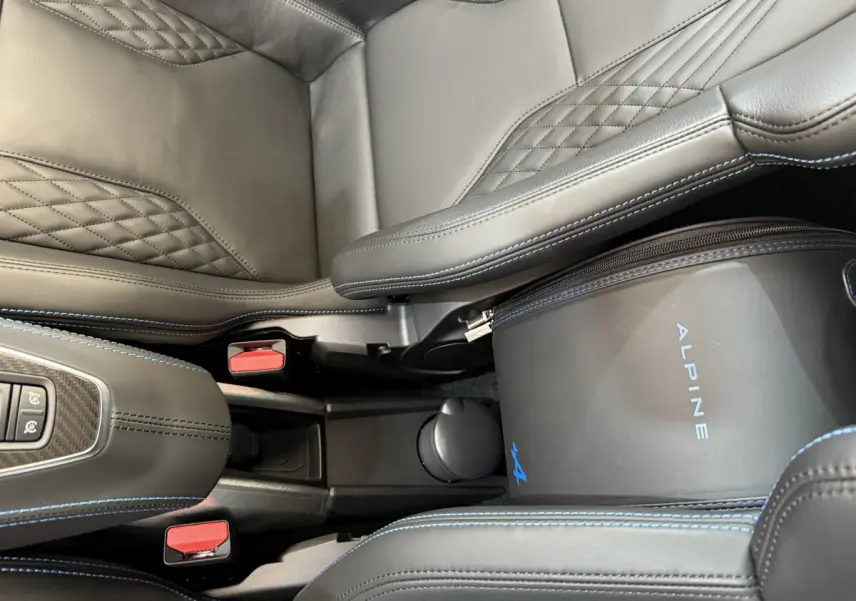 Vue rapprochée de l'intérieur noir avec surpiqûres bleues et sac Alpine entre les sièges de l'Alpine A110 Legende.