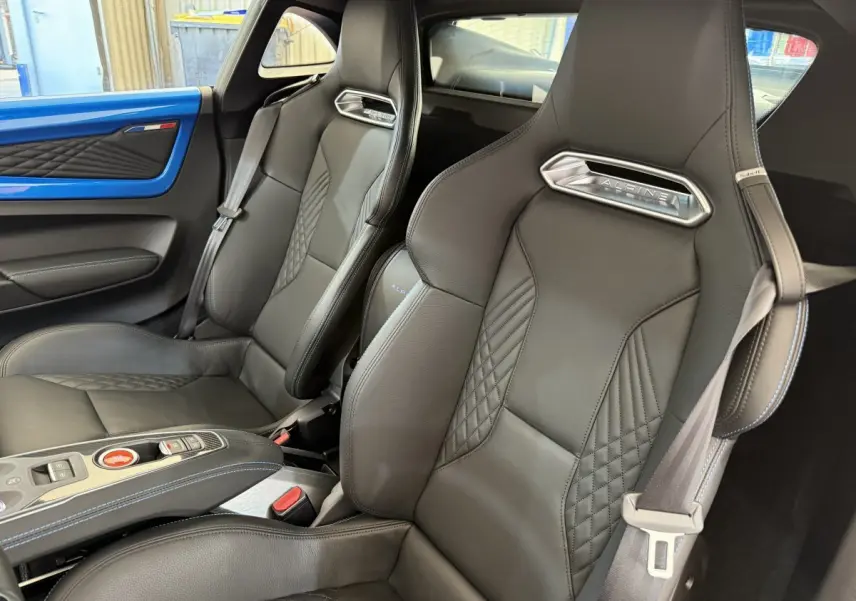 Vue intérieure rapprochée des sièges en cuir noirs de l'Alpine A110 Legende avec détails bleus sur la portière bleue.