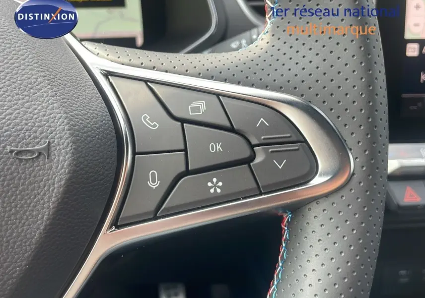 Gros plan sur les commandes à gauche du volant perforé avec surpiqûres tricolores du Renault Captur E-Tech hybride gris cassiopée.