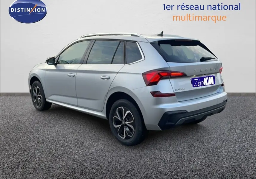 Vue 3/4 arrière droite d'un Skoda Kamiq gris argent métallisé avec jantes bi-ton et toit équipé de barres de toit.