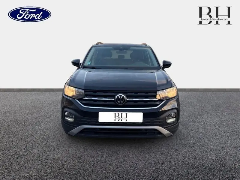 Vue avant d'un Volkswagen T-Cross noir intense nacré avec calandre chromée et phares allumés sur fond neutre.