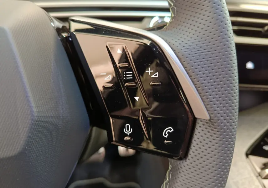 Gros plan sur les commandes tactiles noires du volant cuir perforé côté gauche du Peugeot 3008 blanc hybride 2025.