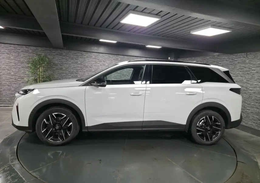 Profil droit du Peugeot 5008 blanc 2025 avec jantes alliage noires et barres de toit noires brillantes.