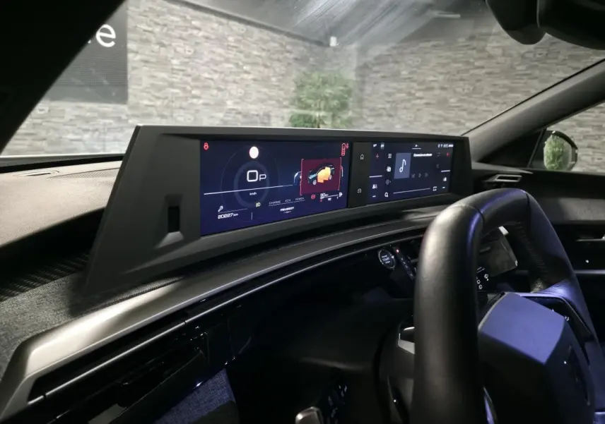 Vue intérieure côté conducteur du tableau de bord numérique et écran tactile du Peugeot 5008 blanc hybride 2025.