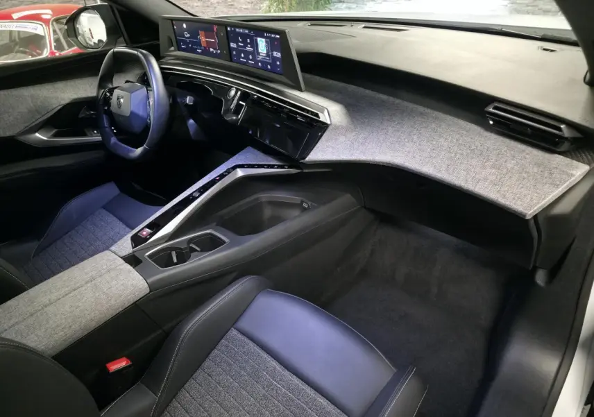 Intérieur avant droit du Peugeot 5008 blanc 2025, tableau de bord tissu gris, double écran HD panoramique et volant compact noir.
