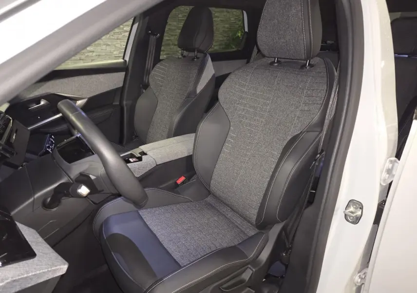 Vue intérieure côté conducteur du Peugeot 5008 blanc 2025, sièges tissu gris et cuir noir avec surpiqûres contrastées.