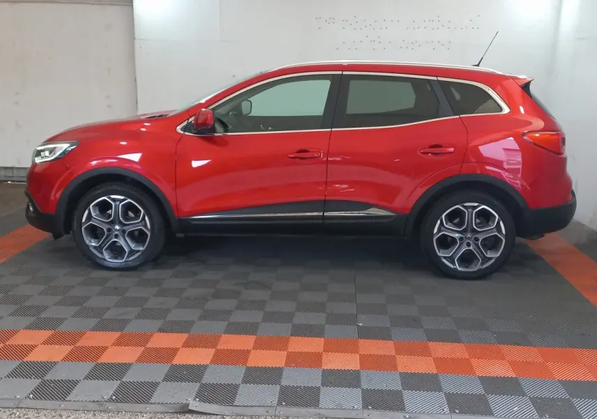 Vue de profil côté gauche d'un Renault Kadjar Intens Energy TCe 130 EDC rouge avec jantes alliage et rails de toit chromés.