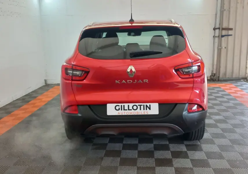 Vue arrière d'un Renault Kadjar rouge avec logo et nom du modèle visibles, dans un garage au sol carrelé noir et orange.