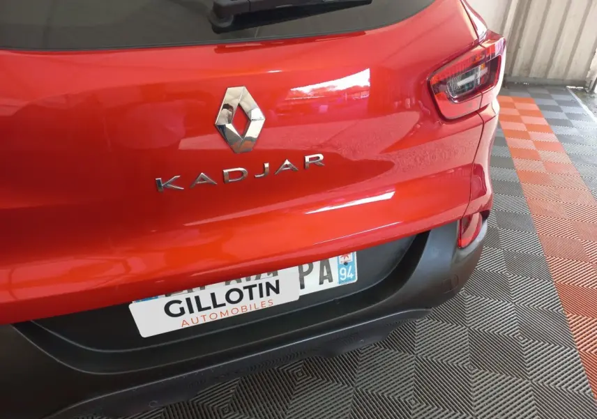 Vue rapprochée arrière d’un Renault Kadjar rouge montrant le logo et le nom du modèle sur un sol à damiers noir et orange.