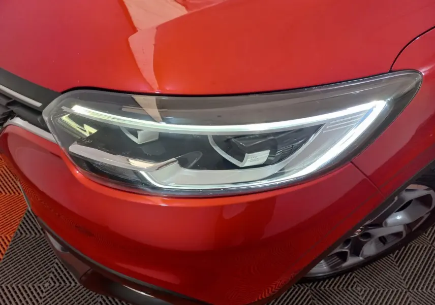 Gros plan sur le phare avant droit du Renault Kadjar rouge, mettant en valeur les feux LED et la calandre chromée.