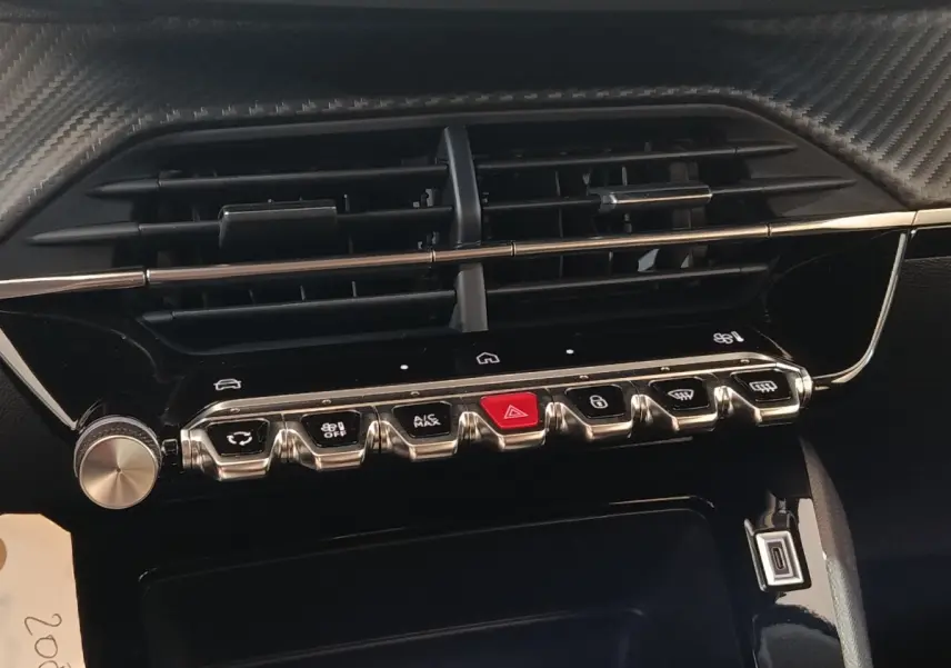 Gros plan sur la console centrale de la Peugeot 208 électrique 2024, boutons de commande et aérateurs noirs.