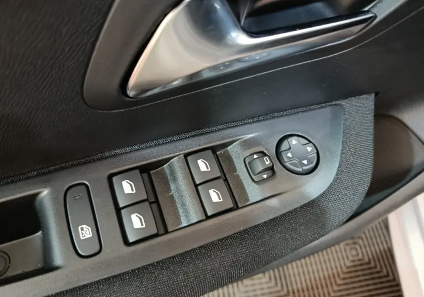 Gros plan sur les commandes de lève-vitres et rétroviseurs côté conducteur d'une Peugeot 208 électrique gris clair.