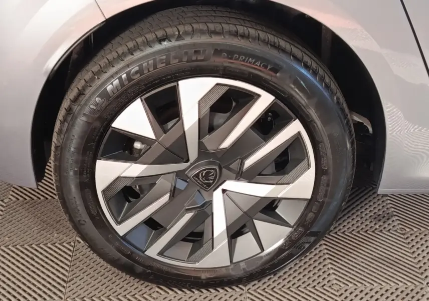 Gros plan sur la roue avant droite d’une Peugeot 208 électrique gris clair avec jante au design géométrique bicolore.