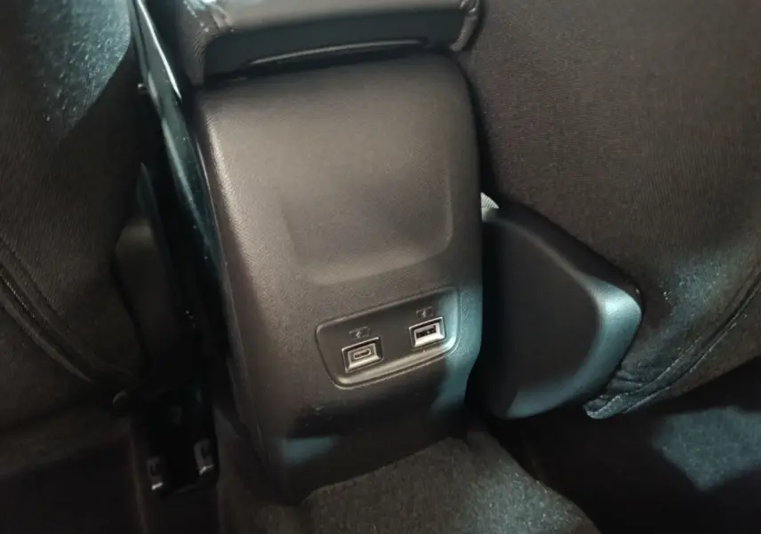 Vue rapprochée des ports USB arrière noirs entre les sièges arrière d'une Peugeot 208 électrique gris clair.