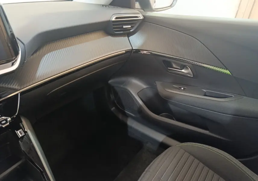 Intérieur côté passager du Peugeot 208 électrique 2024, tableau de bord gris avec finition carbone et siège tissu noir.