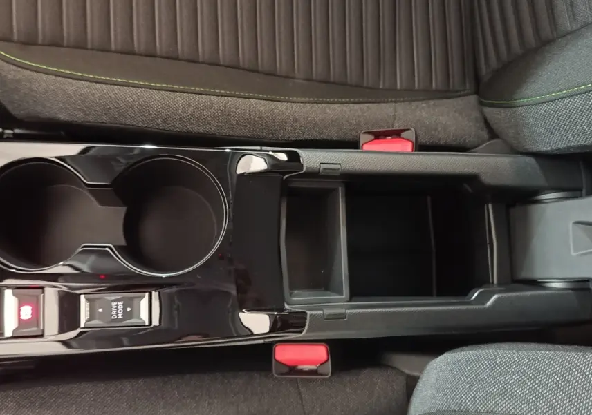 Vue plongeante sur la console centrale noire brillante et les sièges gris avec surpiqûres vertes d'une Peugeot 208 électrique 2024.
