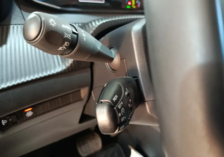 Gros plan sur la commande multifonctions et le commodo d’éclairage du tableau de bord d’une Peugeot 208 électrique blanche.