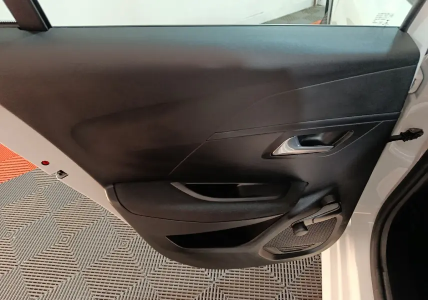 Vue intérieure de la porte arrière droite noire d'une Peugeot 208 électrique blanche, avec poignée et haut-parleur intégrés.