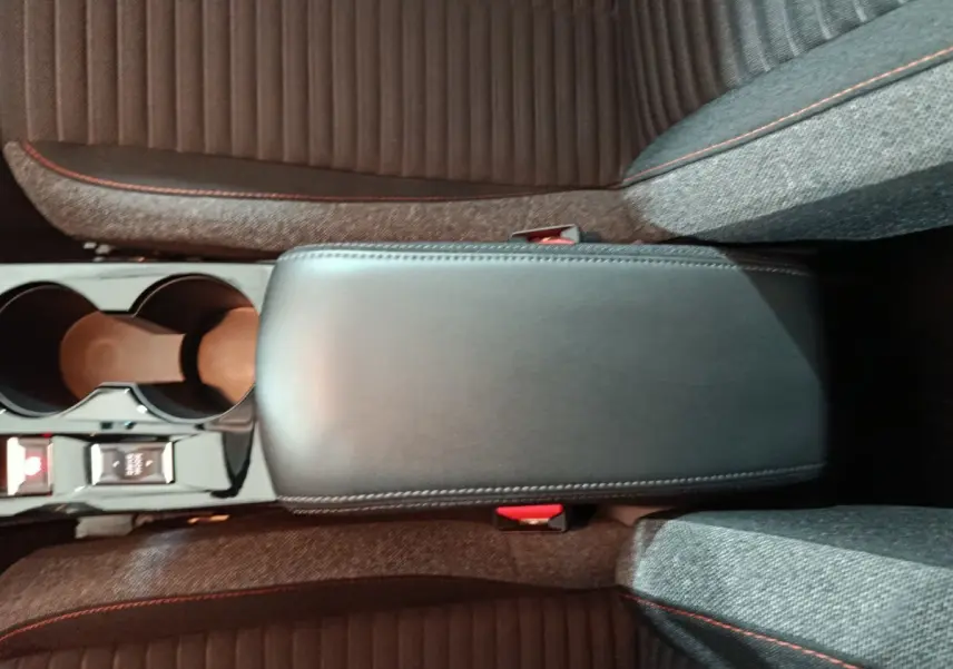 Vue plongeante sur l'accoudoir central noir et les sièges gris avec surpiqûres rouges de la Peugeot 208 Electrique Active Business.