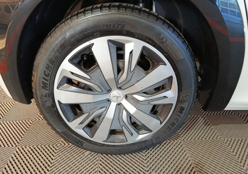 Gros plan sur la roue avant droite d'une Peugeot 208 électrique blanche avec jante spécifique et pneu Michelin.