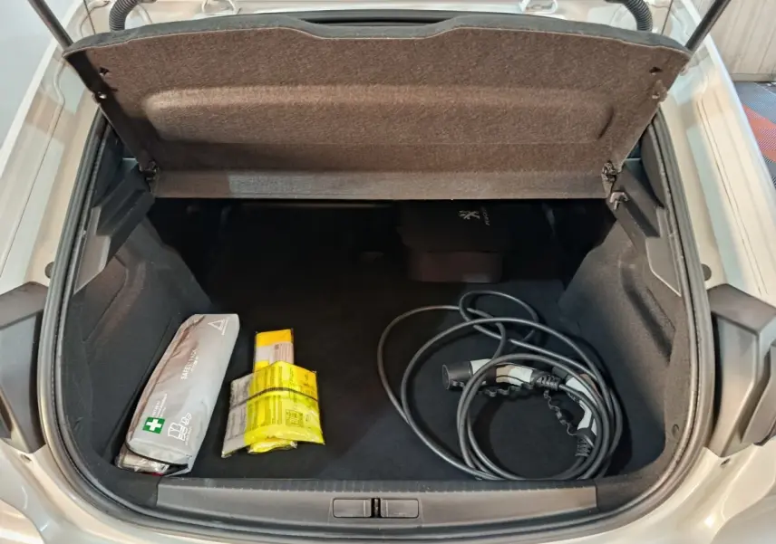 Coffre ouvert vu de dessus d’une Peugeot 208 Electrique Active Business blanche avec câble de recharge et kit de sécurité.