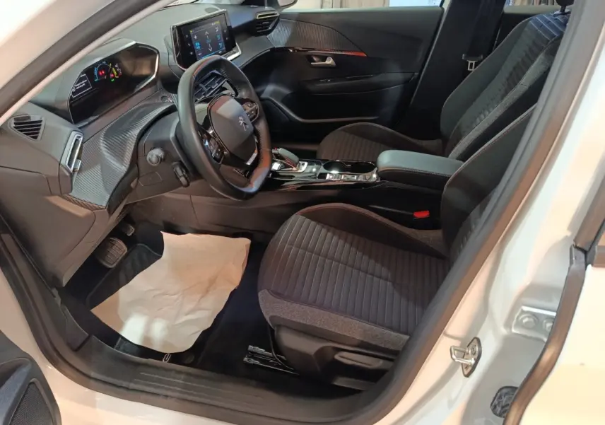 Vue intérieure côté conducteur de la Peugeot 208 électrique blanche, volant cuir multifonctions et écran tactile central visible.