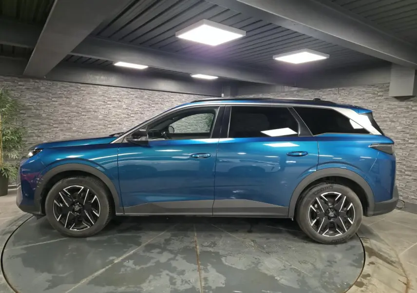 Profil droit d'un Peugeot 5008 bleu métallisé 2025 avec jantes alliage 19'' noires et barres de toit noires brillantes.