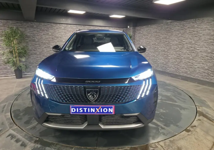 Peugeot 5008 bleu métallisé vue de face, avec calandre noire et feux LED à trois griffes allumés.