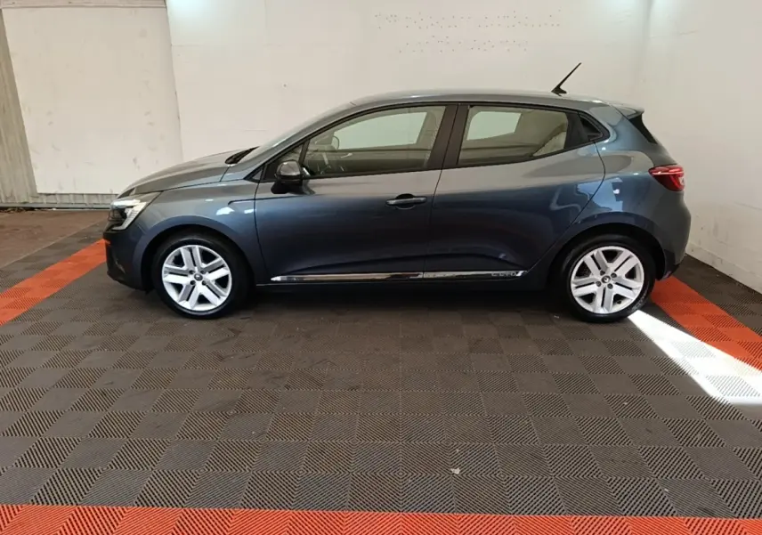 Profil droit d'une Renault Clio Business TCe 100 gris foncé, avec jantes alliage et toit compact dans un garage.