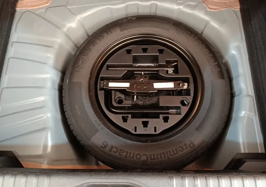 Vue plongeante sur la roue de secours et son kit d'outils dans le coffre d'une Renault Clio Business gris foncé.