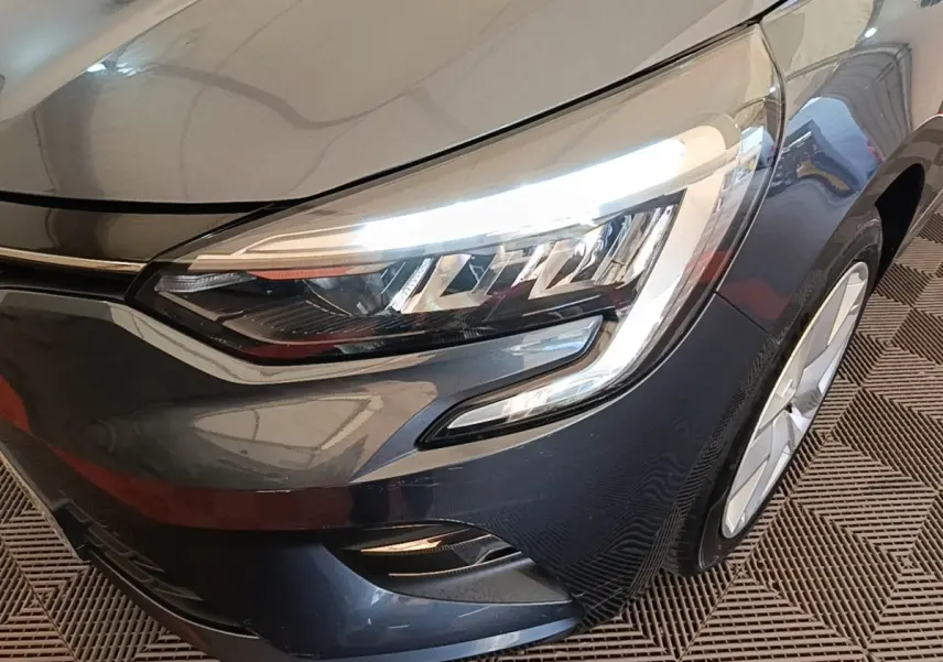 Gros plan sur l'avant droit gris foncé de la Renault Clio 2021 avec ses phares LED allumés et jante visible.