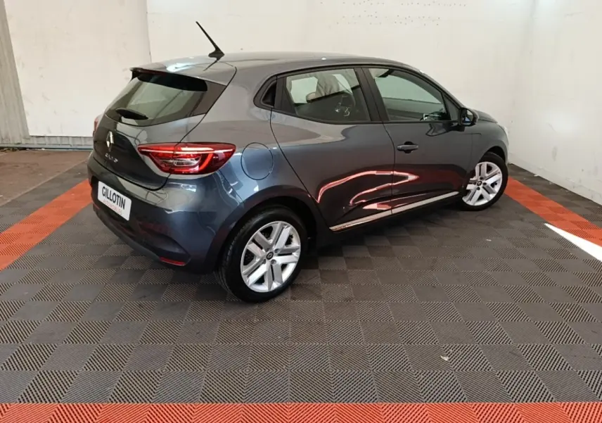 Renault Clio Business TCe 100 gris foncé vue 3/4 arrière droit dans un espace intérieur avec sol à damier noir et orange.
