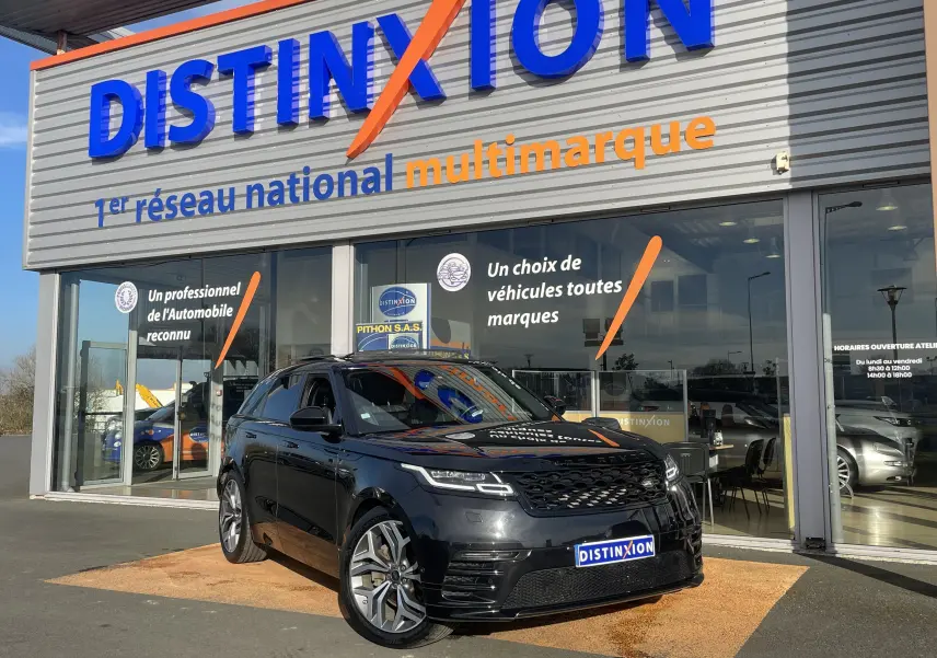 Range Rover Velar noir Santorini en 3/4 avant droit, garé devant une concession Distinxion avec logo visible.